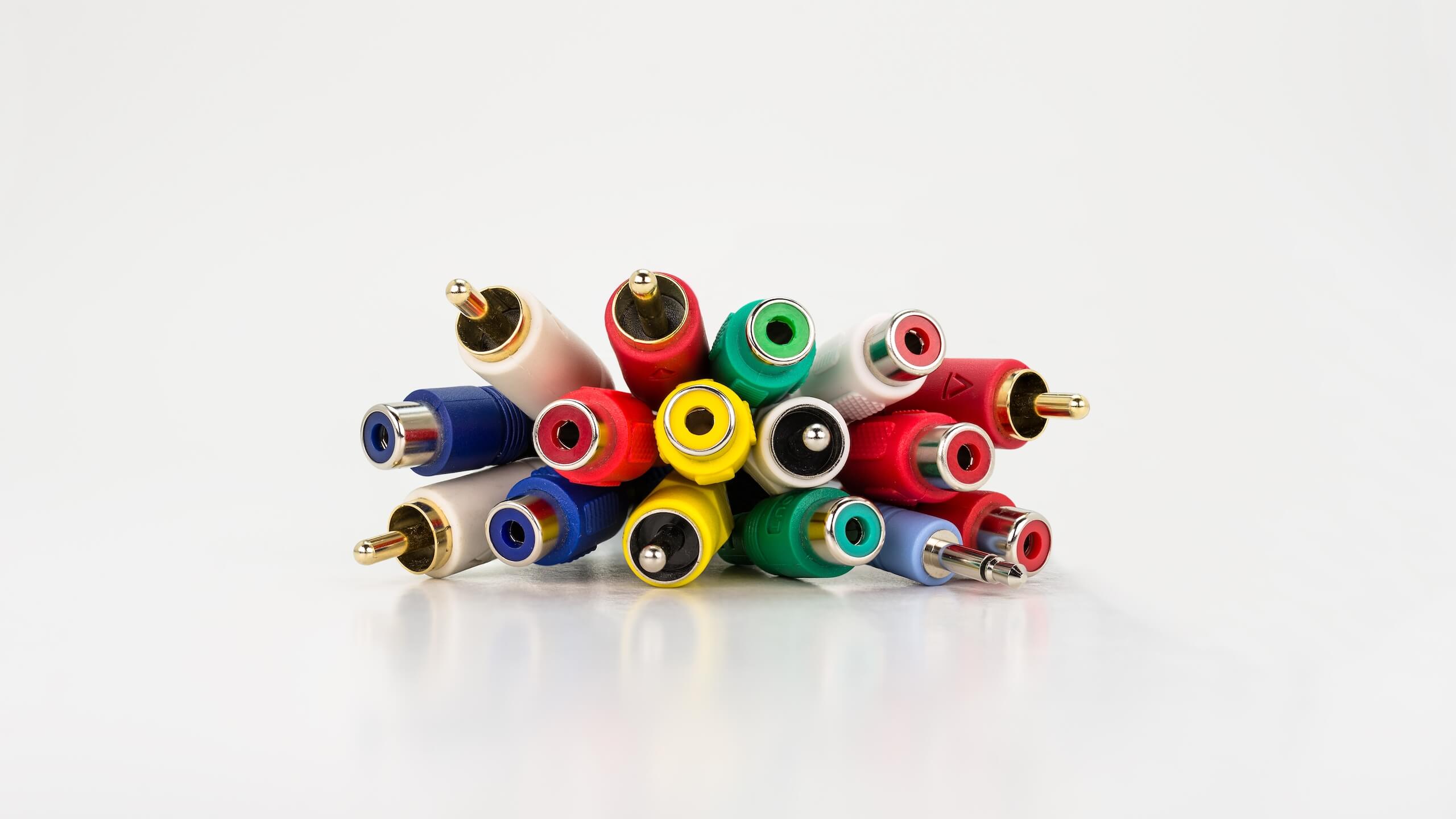 A bundle of colorful RCA cables are neatly arranged and placed together, with their connectors pointing outward. The vibrant cables and connectors in red, yellow, green, blue, and white reflect on a smooth white surface, perfect for any TV wall mounting setup.