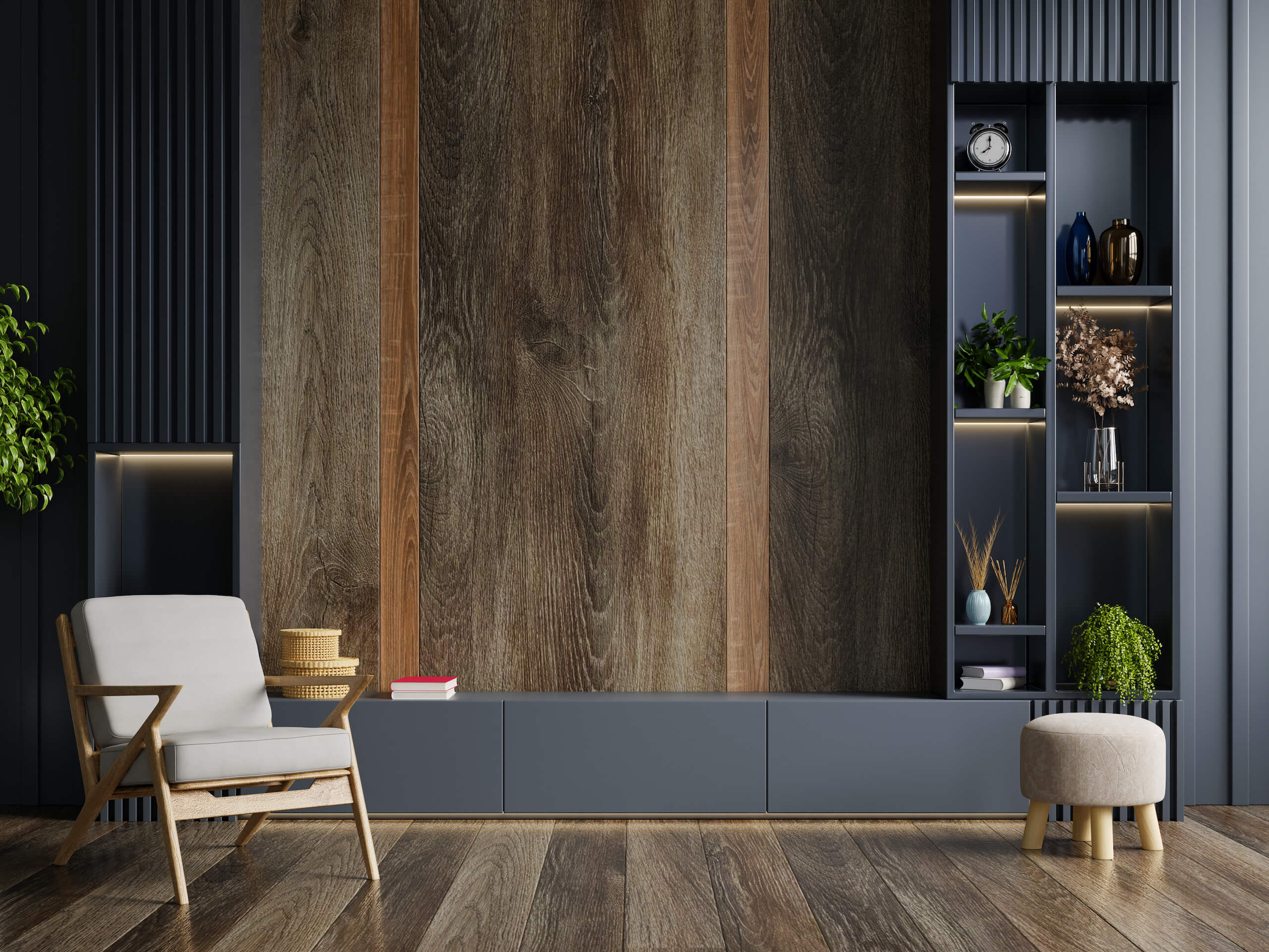 A modern living room featuring a wooden accent wall with built-in shelves and a TV wall mounting. The shelves display various decorative items, including plants and books. A cushioned wooden chair with a small wooden table and a round ottoman are placed on the wooden floor.