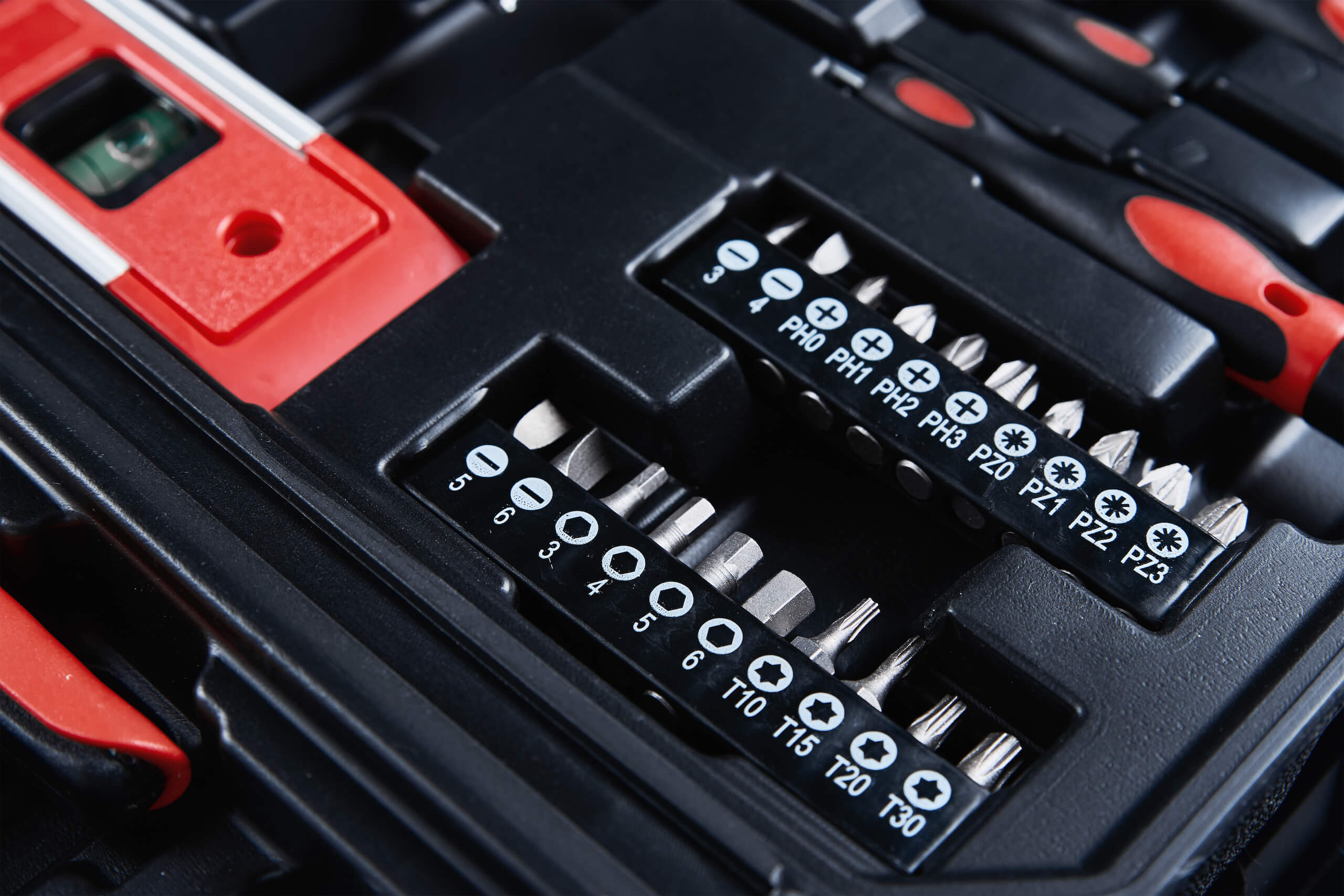 A detailed close-up view of a toolbox with various screwdriver bits, including flat, Phillips, and Torx, neatly organized in labeled slots. Perfect for TV wall mounting, the tool set also features a red spirit level in the top left corner of the image.